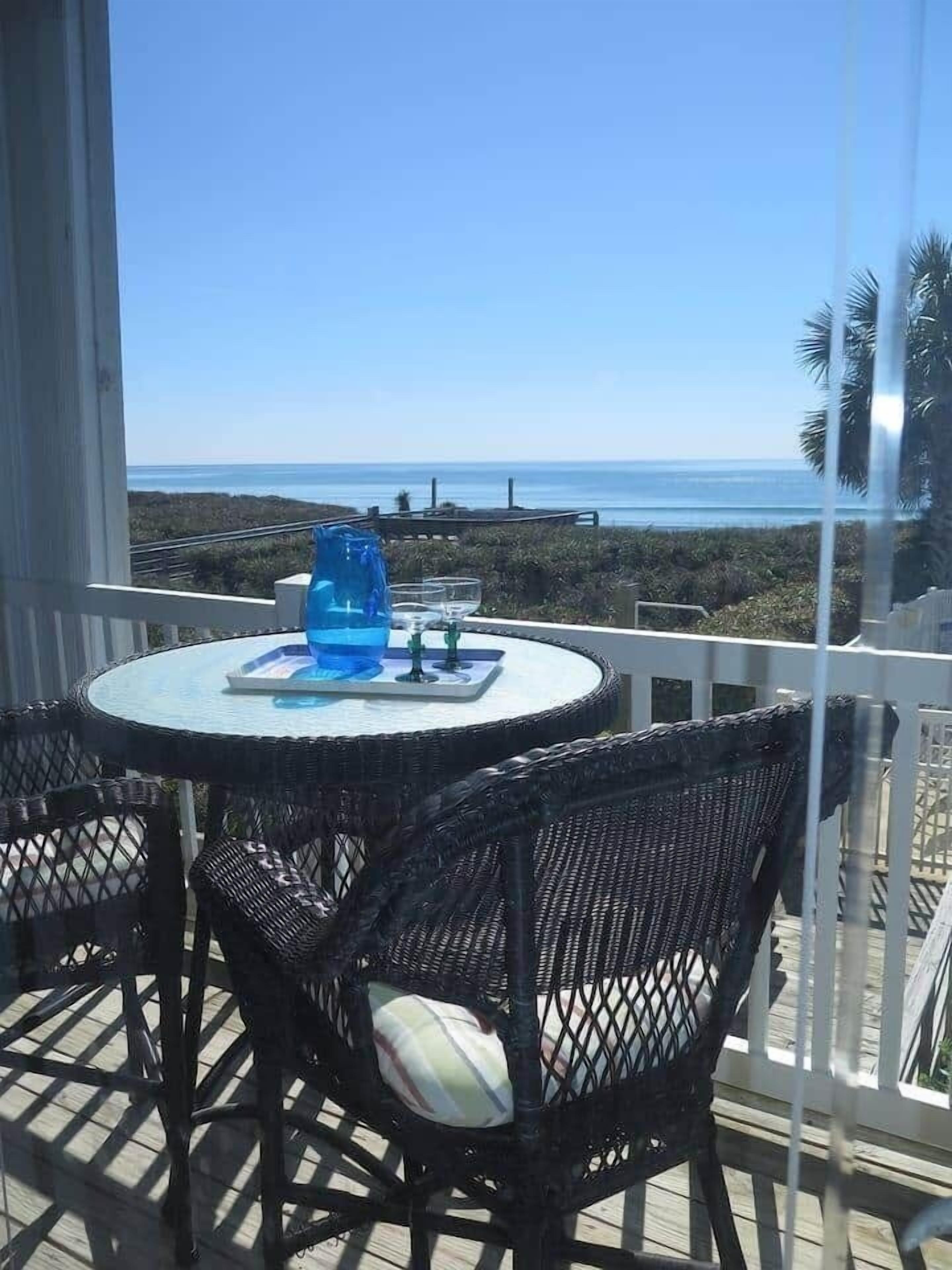 A round table with chairs on a balcony overlooking the ocean.