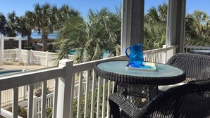 A balcony with a round table, a blue vase, and a view of palm trees and a pool.