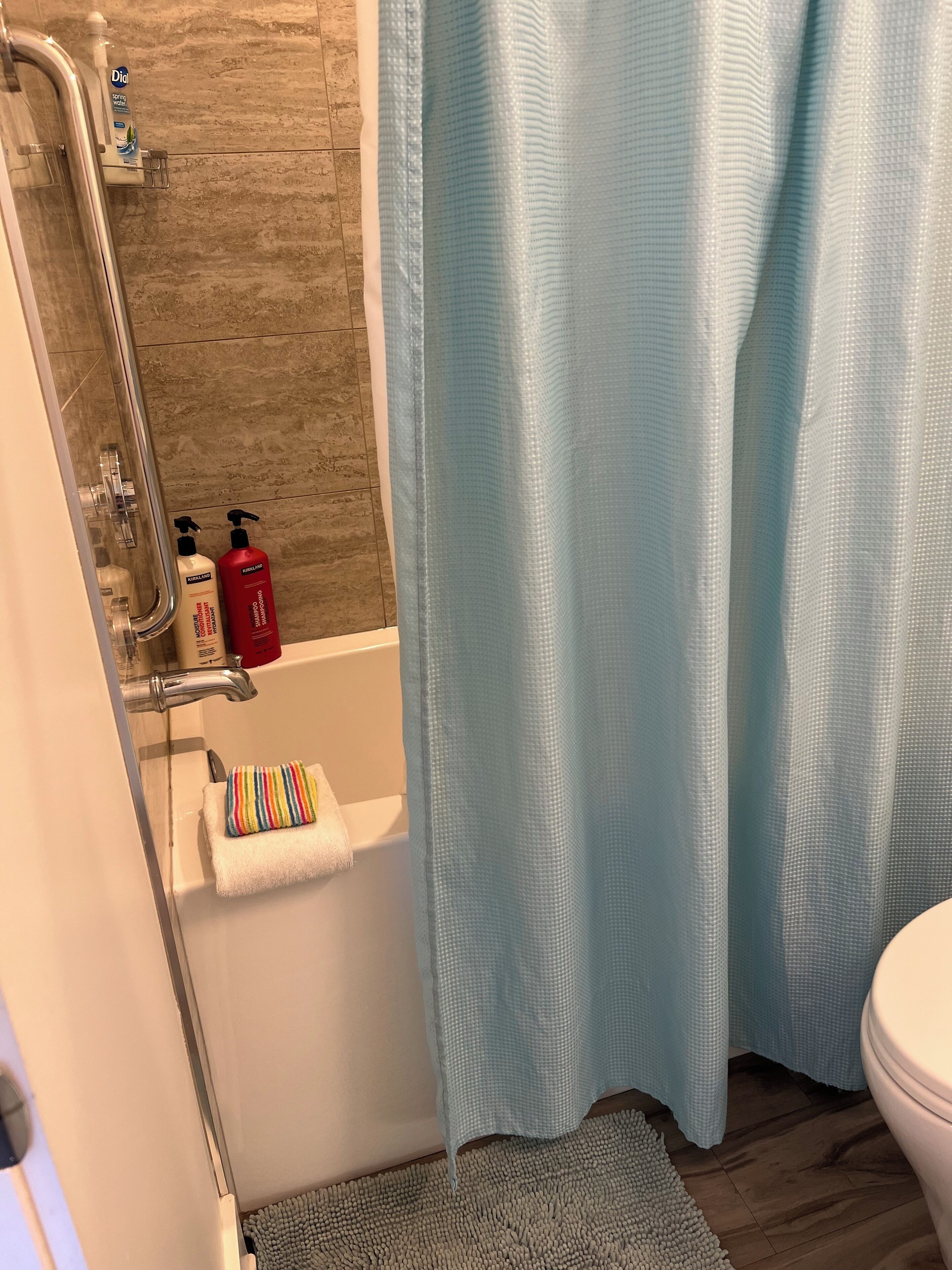 Une salle de bain avec une douche, une baignoire et des toilettes. Deux bouteilles de shampoing et d’après-shampoing sont posées sur le bord de la baignoire.