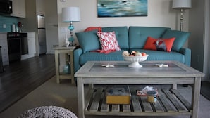 Un salon avec un canapé de couleur turquoise, une table basse et une cuisine en arrière-plan.