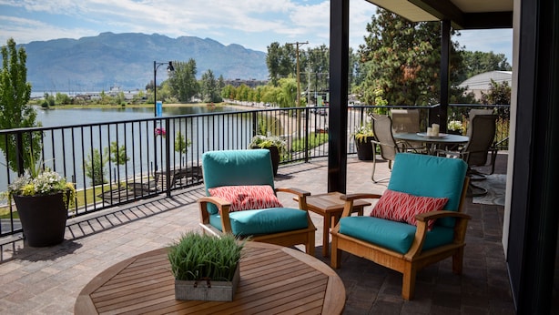 Une terrasse couverte, aménagée avec du mobilier d’extérieur, offrant une vue sur un lac et, au loin, sur des montagnes.