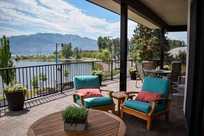 A covered patio with outdoor furniture, a view of a lake, and mountains in the background.