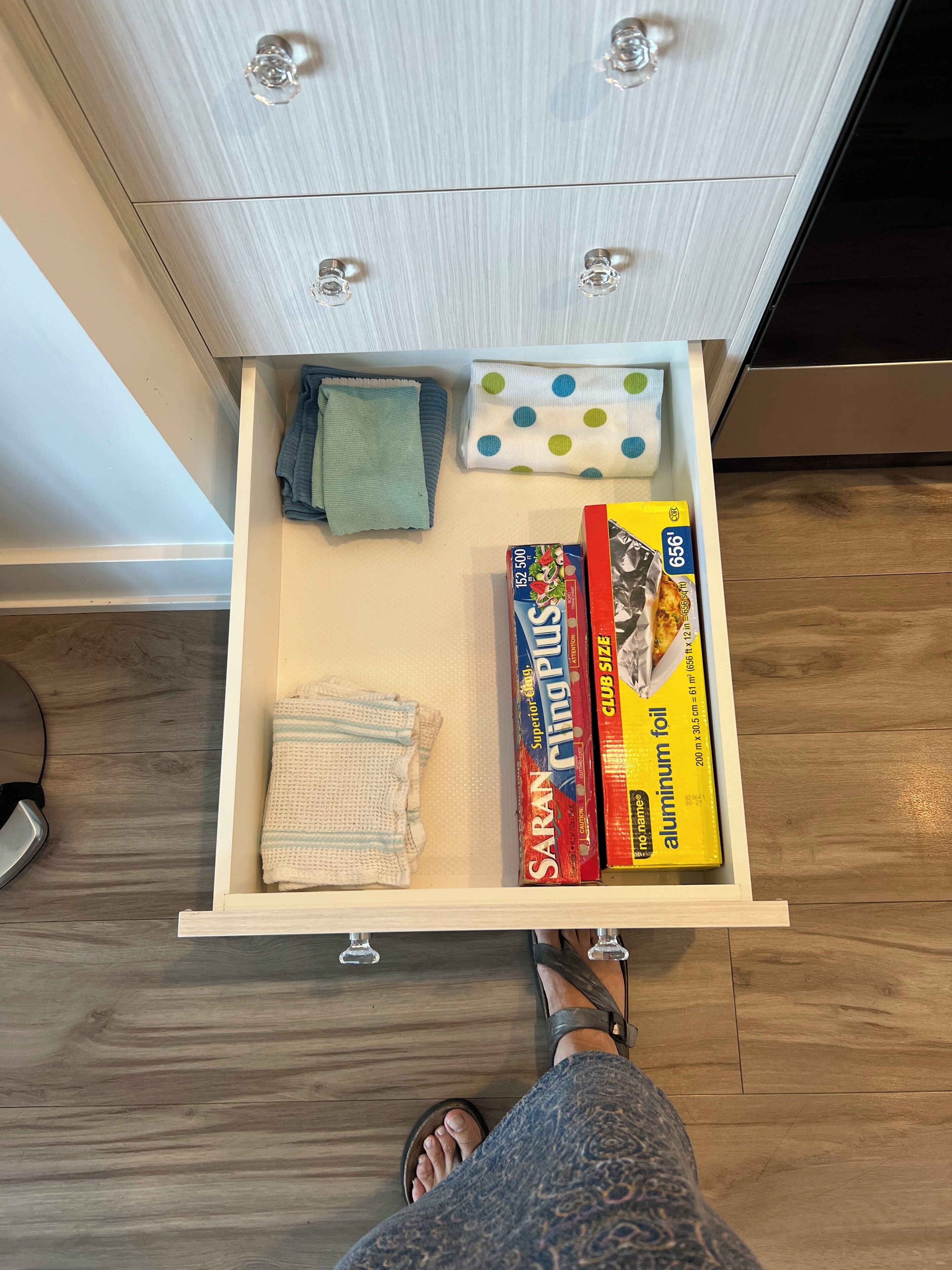 A drawer with kitchen items including aluminum foil, a cloth, and a box of club size aluminum foil.