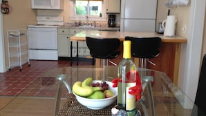 A kitchen with white cabinets, a microwave, and a refrigerator. There is a dining table with chairs and a bowl of fruit on it.