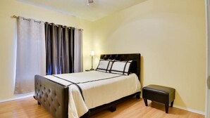 A bedroom with a bed, a nightstand, a lamp, a ceiling fan, and a window with curtains. - Beautiful Condo Near The Domain (Austin)