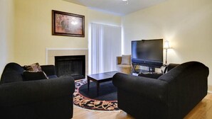 A living room with a fireplace, a ceiling fan, a TV, and two sofas. - Beautiful Condo Near The Domain (Austin)