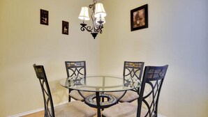 A dining area with a glass table surrounded by four chairs with intricate back designs. - Beautiful Condo Near The Domain (Austin)