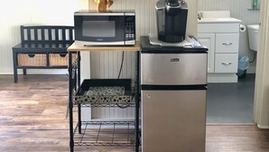 Kompakti keittiö, jossa on mikroaaltouuni, kahvinkeitin ja jääkaappi. Näkyvissä on pieni pöytä, jonka päällä on pyyhe ja seinälle ripustettuja keittiövälineitä.