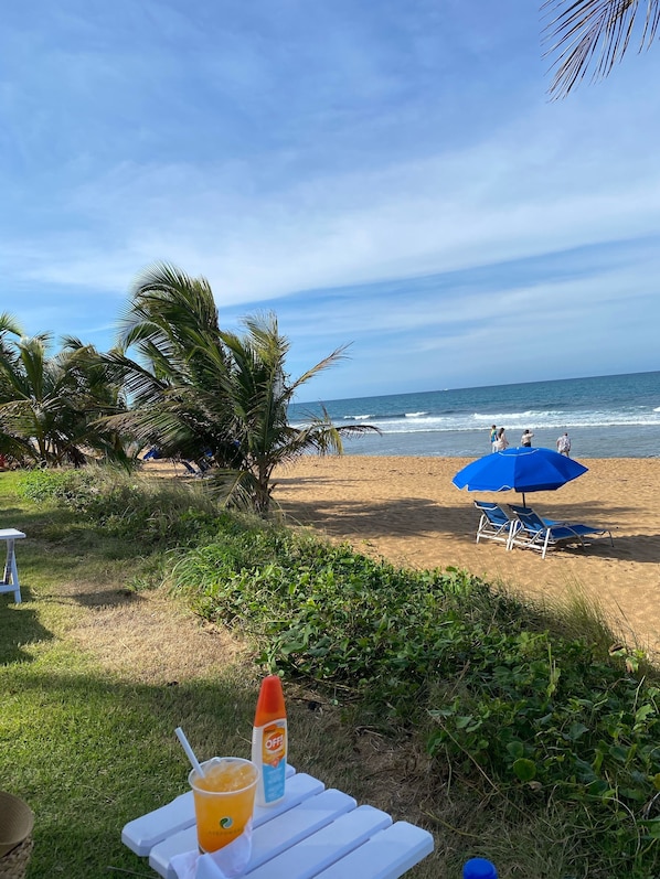 A beachside table with a drink and sunscreen, a blue umbrella, and a chair. - Walk to beach and restaurants bars and Full Power Generator free gated parking (San Juan)