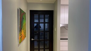 Un pasillo con suelo de baldosas, una puerta con marco negro y un cuadro en la pared.