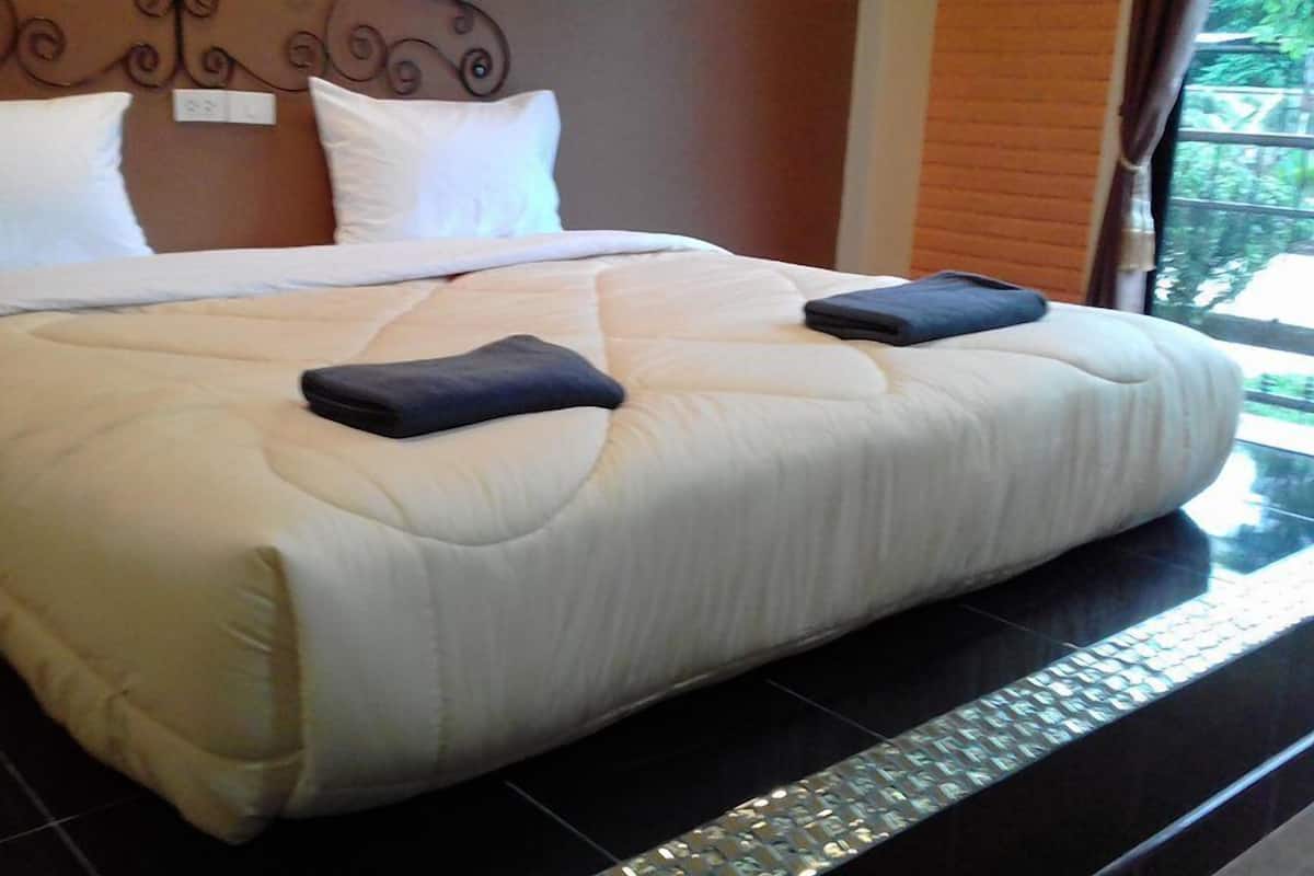 A hotel room with a large bed, a headboard with a decorative design, and a window with a view of greenery outside.