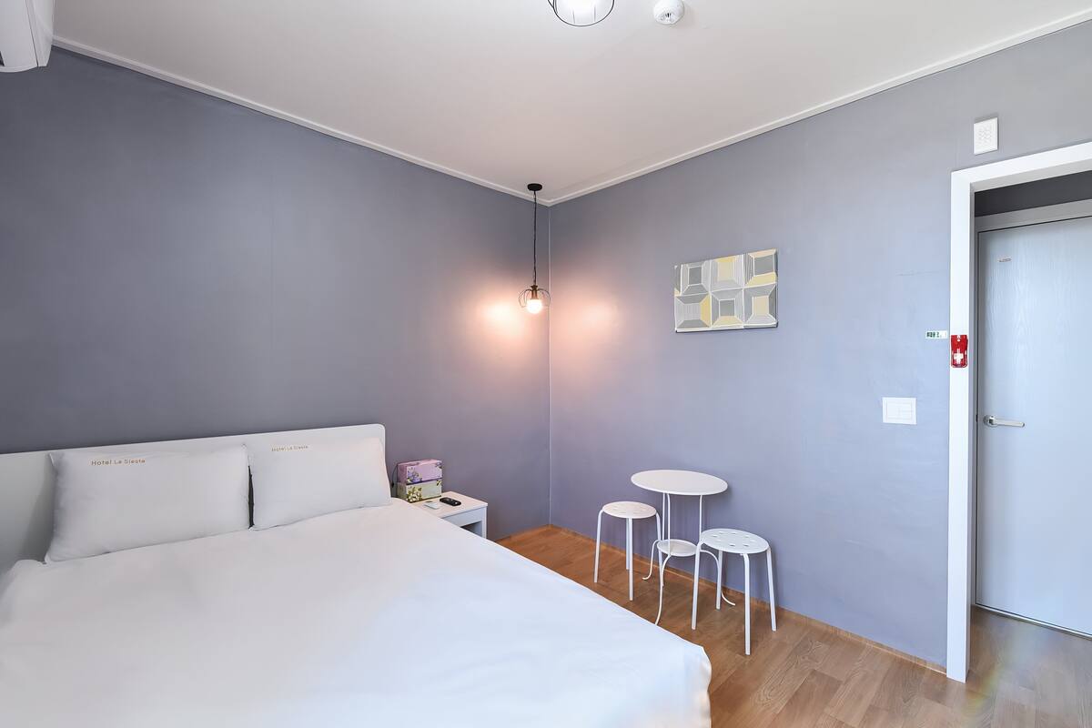A hotel room with a large bed, a bedside table, a small table with chairs, and a door.