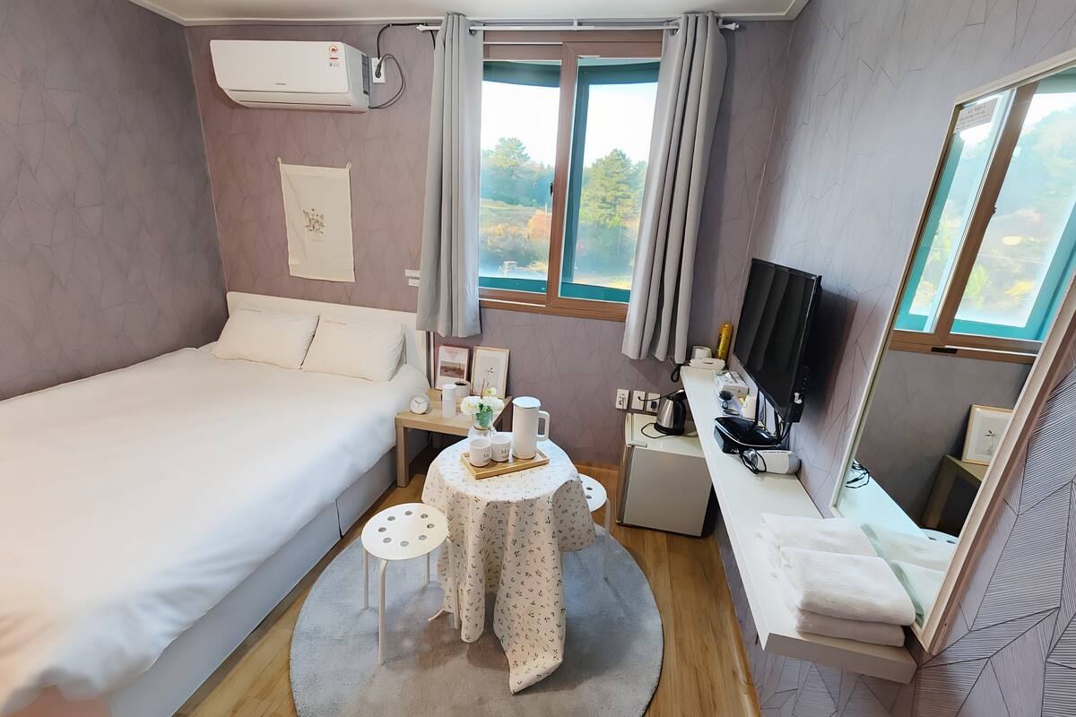 A bedroom with a bed, bedside table, TV, and a window with curtains.