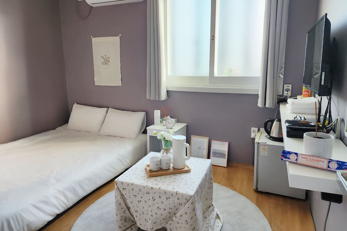 A neatly arranged hotel room with a bed, a small table with a tray of items, a desk with a computer and a television, and a window with curtains.