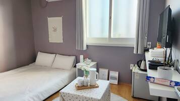 A neatly arranged hotel room with a bed, a small table with a tray of items, a desk with a computer and a television, and a window with curtains.