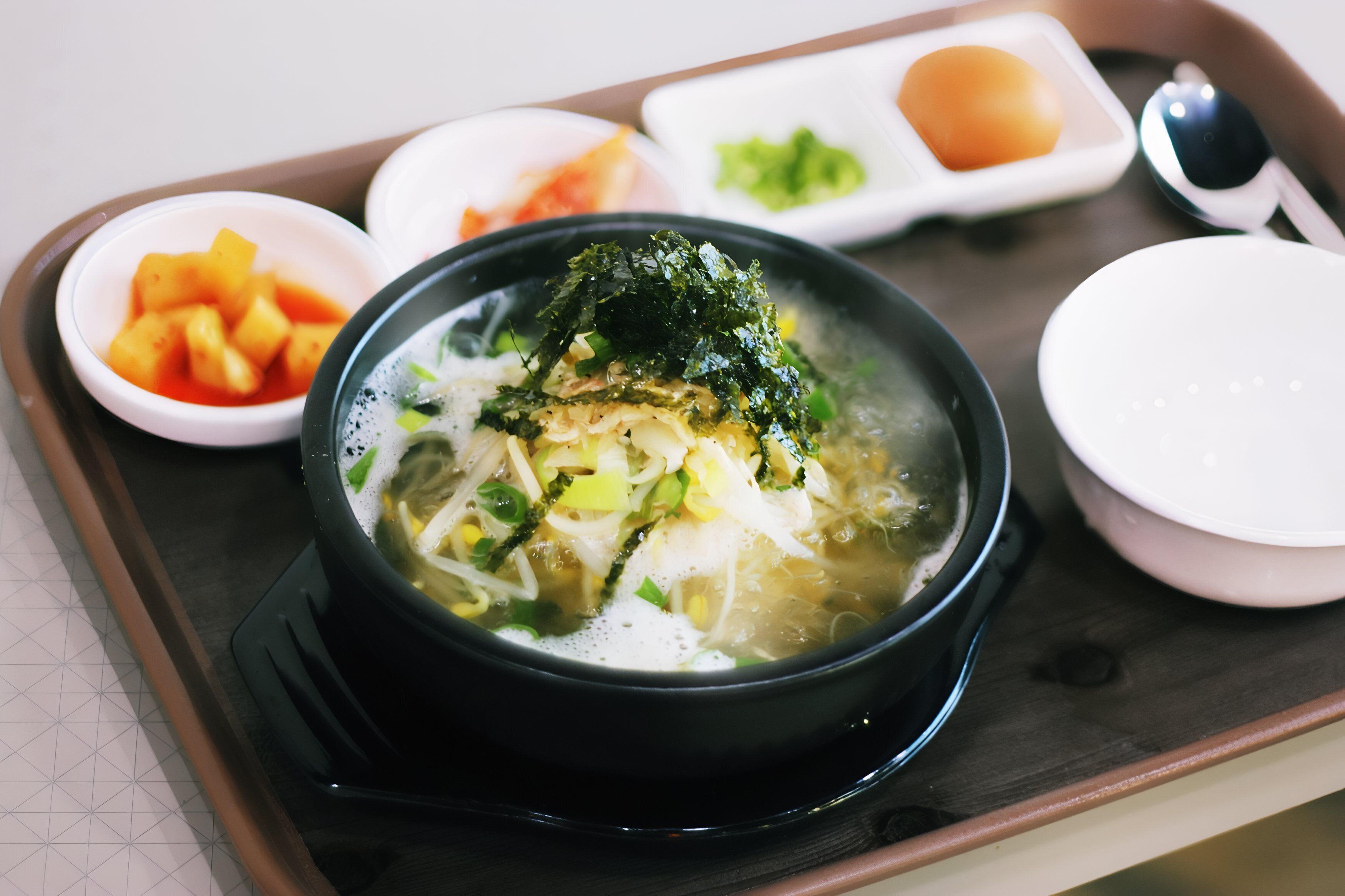A bowl of soup with seaweed and vegetables on a tray with other food items.