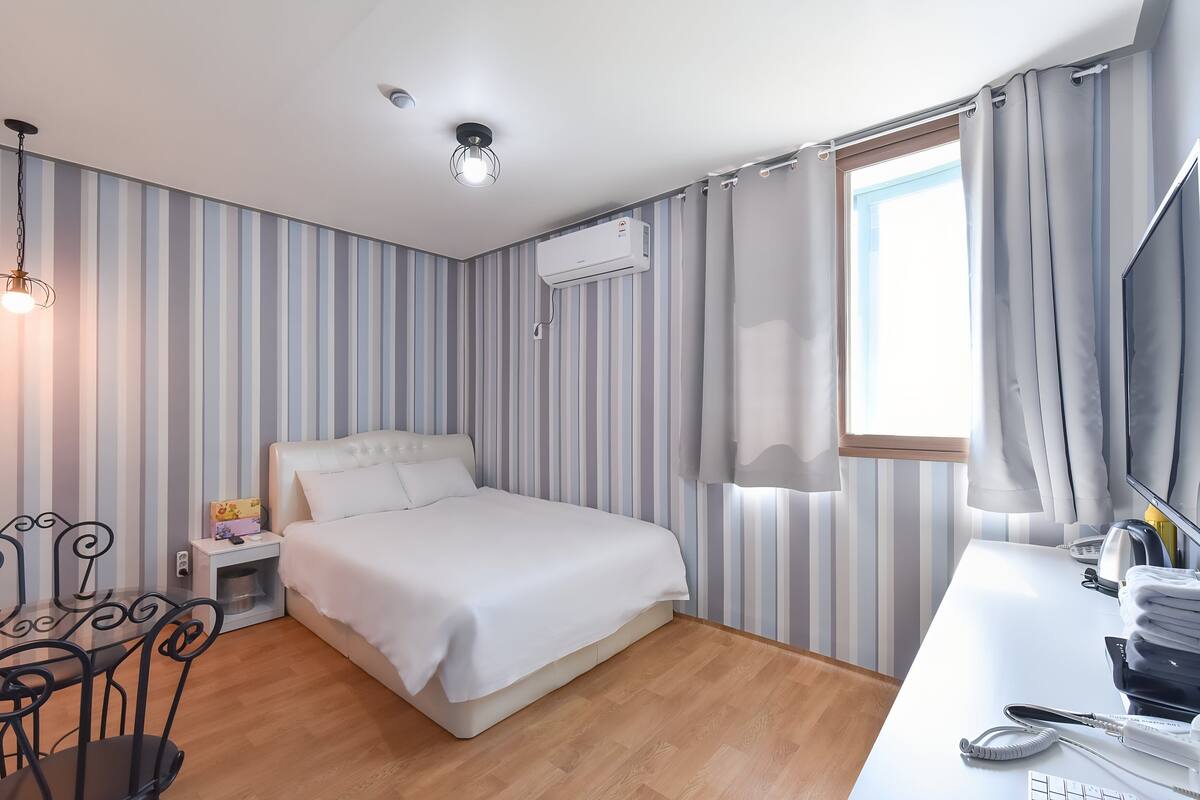 A hotel room with a bed, bedside table, lamp, curtains, and a window.
