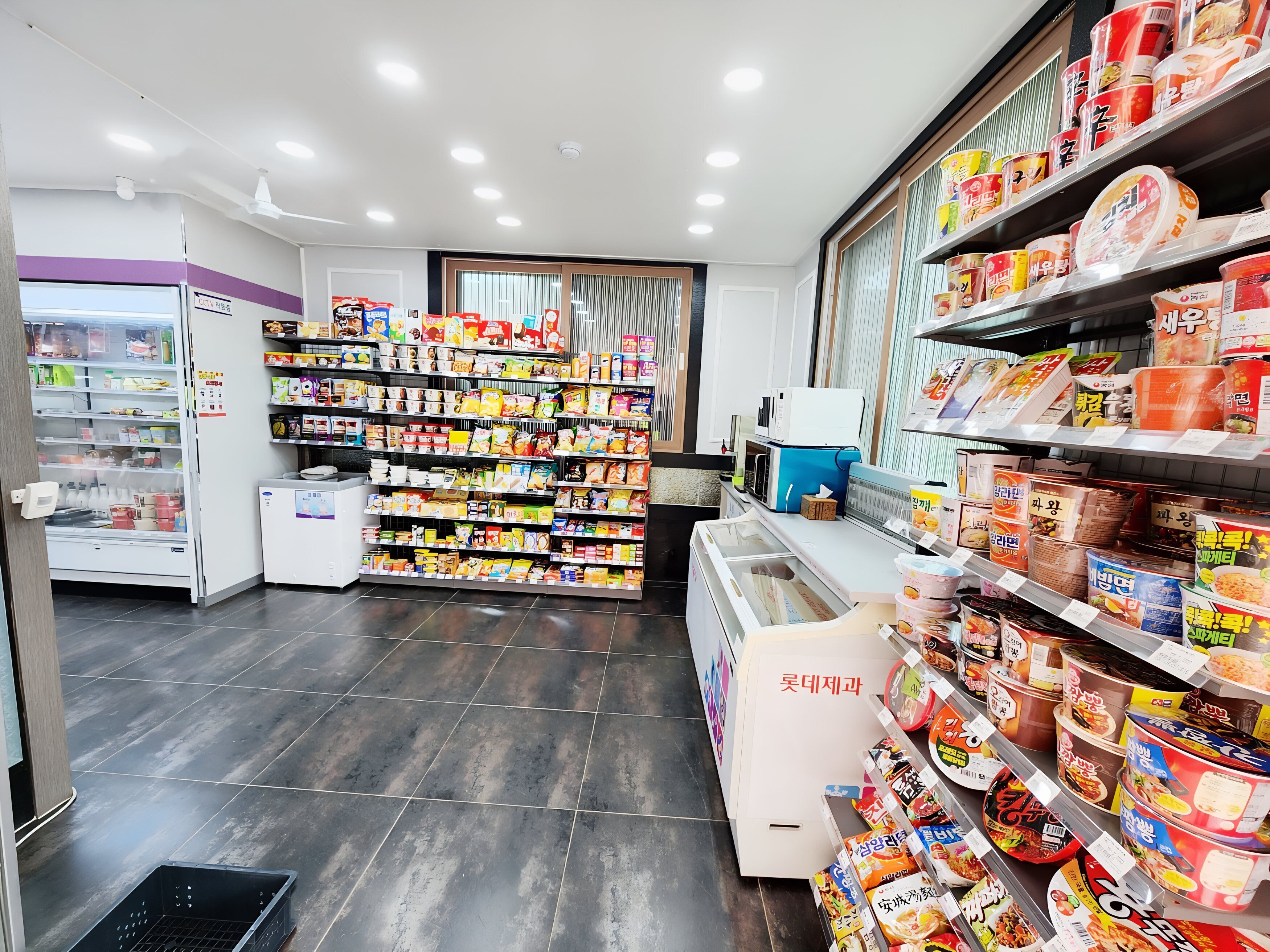 Um supermercado com prateleiras repletas de diversos produtos alimentares, uma área refrigerada e um balcão de atendimento.