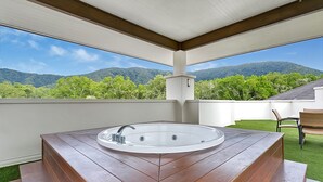 Un bain à remous sur une terrasse en bois, avec vue sur les montagnes et la verdure.