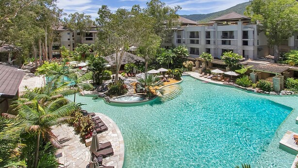 Un complexe hôtelier doté d’une grande piscine, entourée de palmiers et de chaises longues.