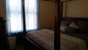 Ein Himmelsbett mit einem gemusterten Bettbezug, ein Nachttisch und ein Papierkorb.