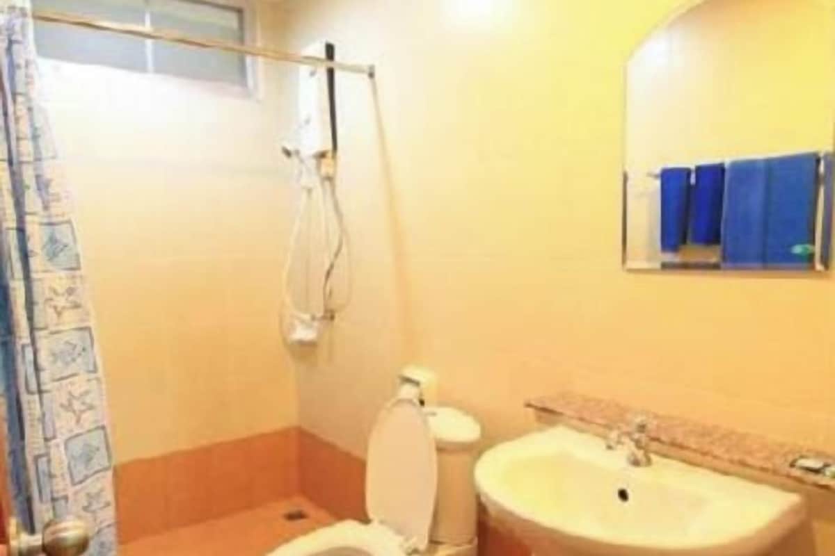 A bathroom with a toilet, sink, shower, and a window with a curtain.