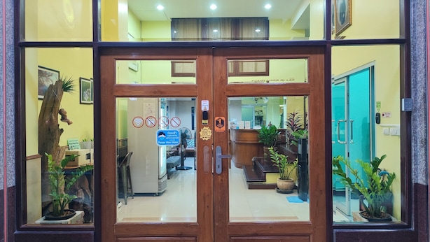 Entrada de hotel com porta dupla de madeira, balcão de recepção e plantas em vasos.