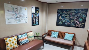 Um hall com dois sofás de madeira, um mapa na parede e um grande cartaz de uma paisagem urbana.