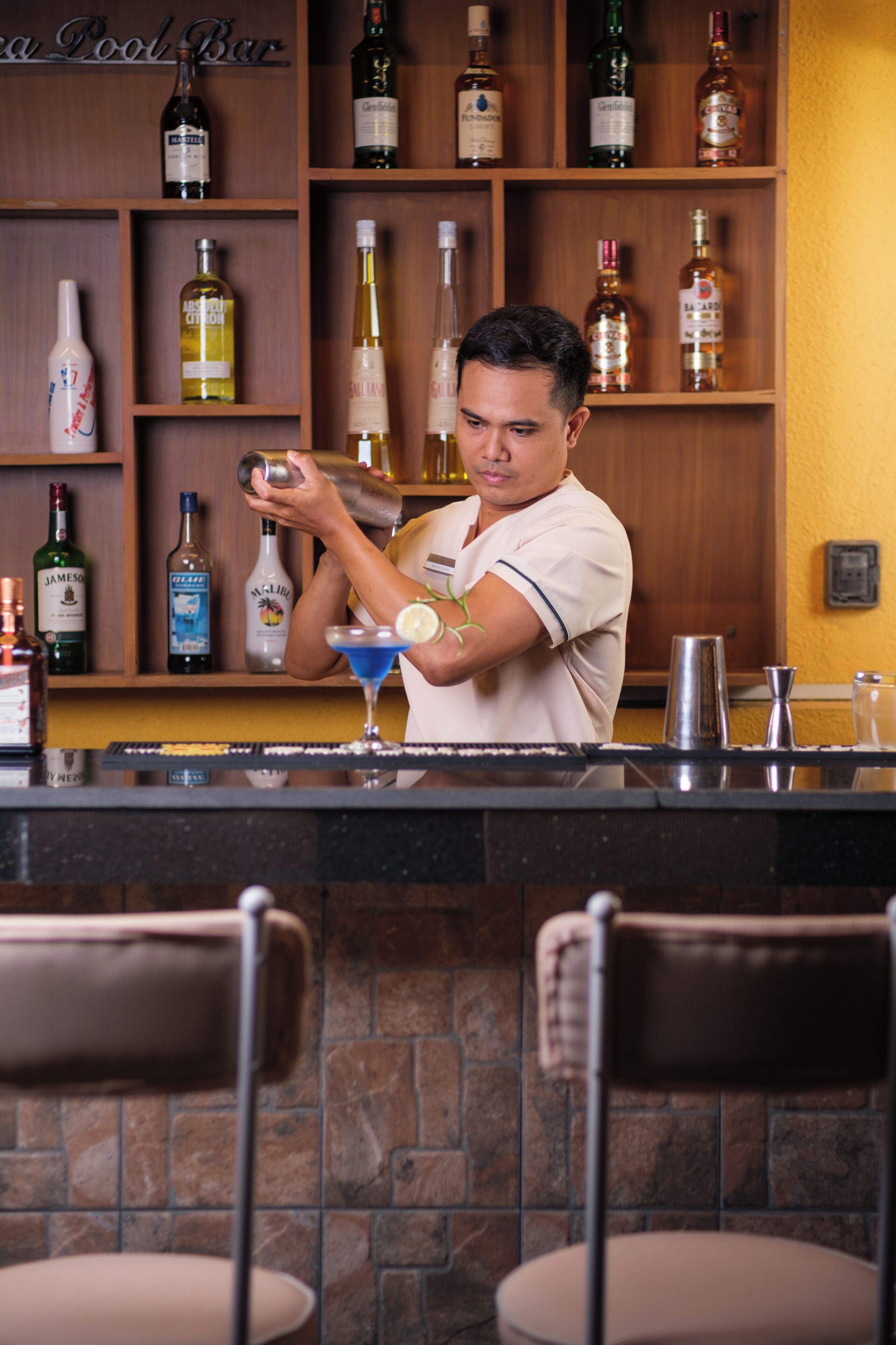 Een bartender achter een bar, met een divers aanbod aan drankflessen op de planken.