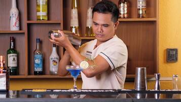 Een bartender achter een bar, met een divers aanbod aan drankflessen op de planken.
