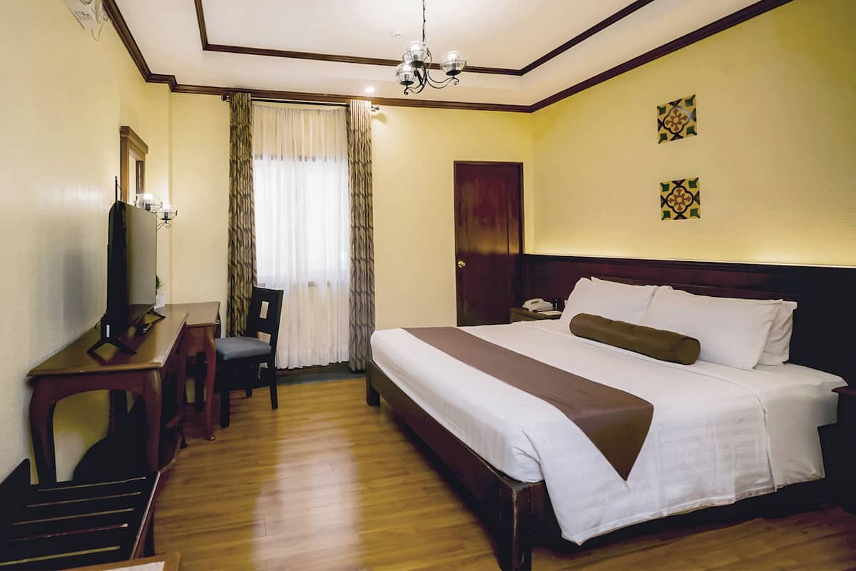 A hotel room with a bed, a desk, a chair, a television, a window with curtains, and a door.