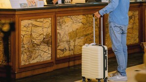 Zona de recepción de un hotel con un mostrador de mármol, relojes, una lámpara y un hombre con una maleta.