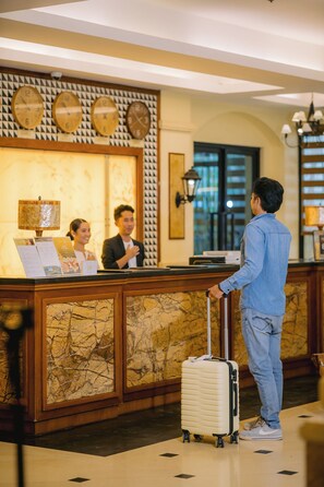 A hotel reception area with a marble reception desk, clocks, a lamp, and a man with a suitcase. - Sunlight Guest Hotel Coron (Coron)