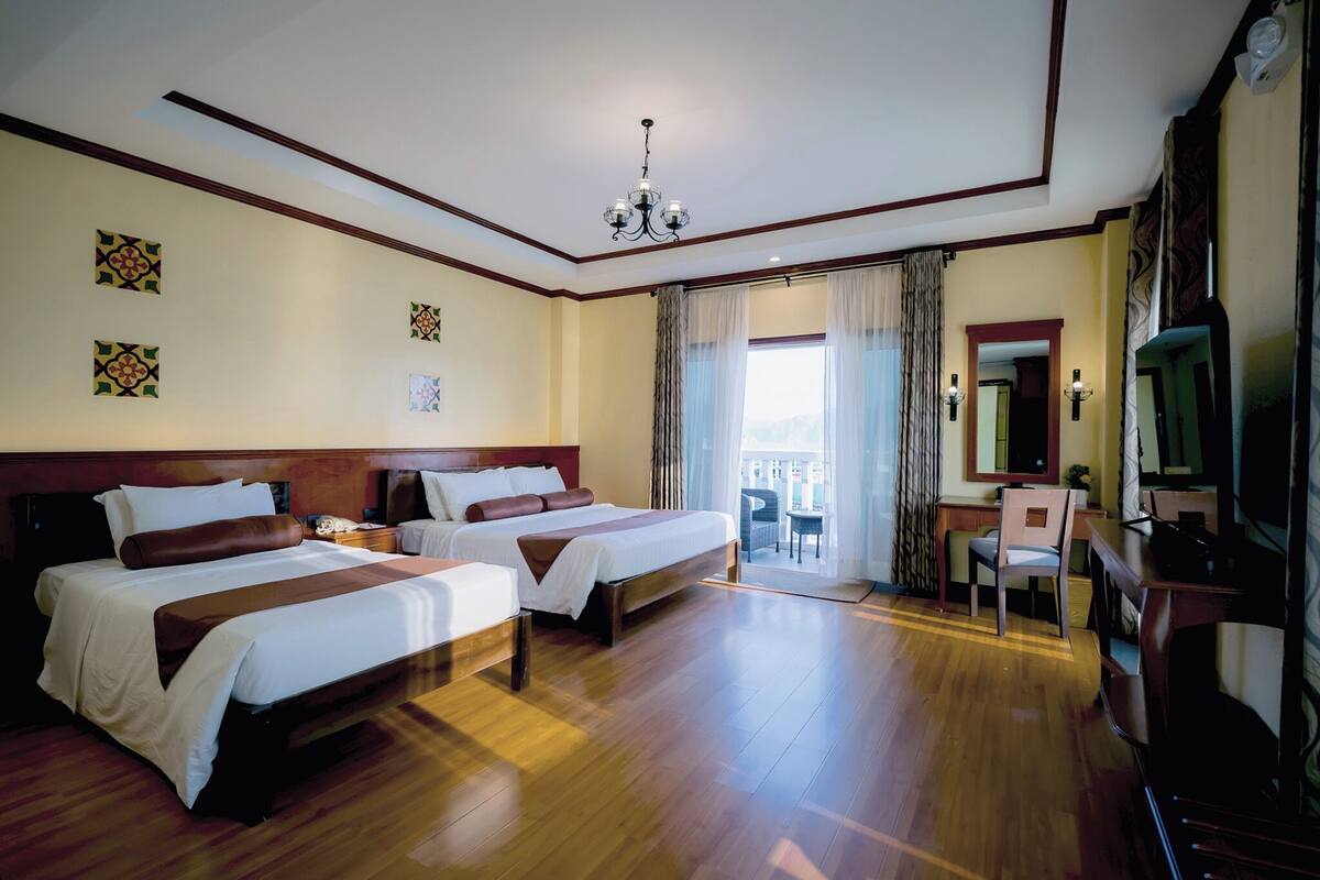 A hotel room with two beds, a desk, a chair, a television, and a balcony with curtains.
