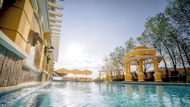 Una piscina con pérgola, sombrillas y sillas de descanso.