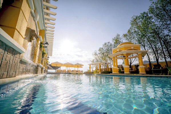 Una piscina con pérgola, sombrillas y sillas de descanso.