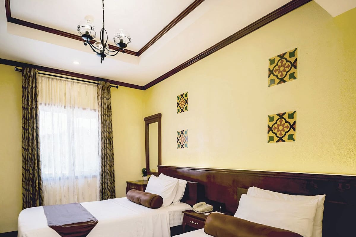 A hotel room with two beds, a chandelier, a mirror, and patterned wall decorations.