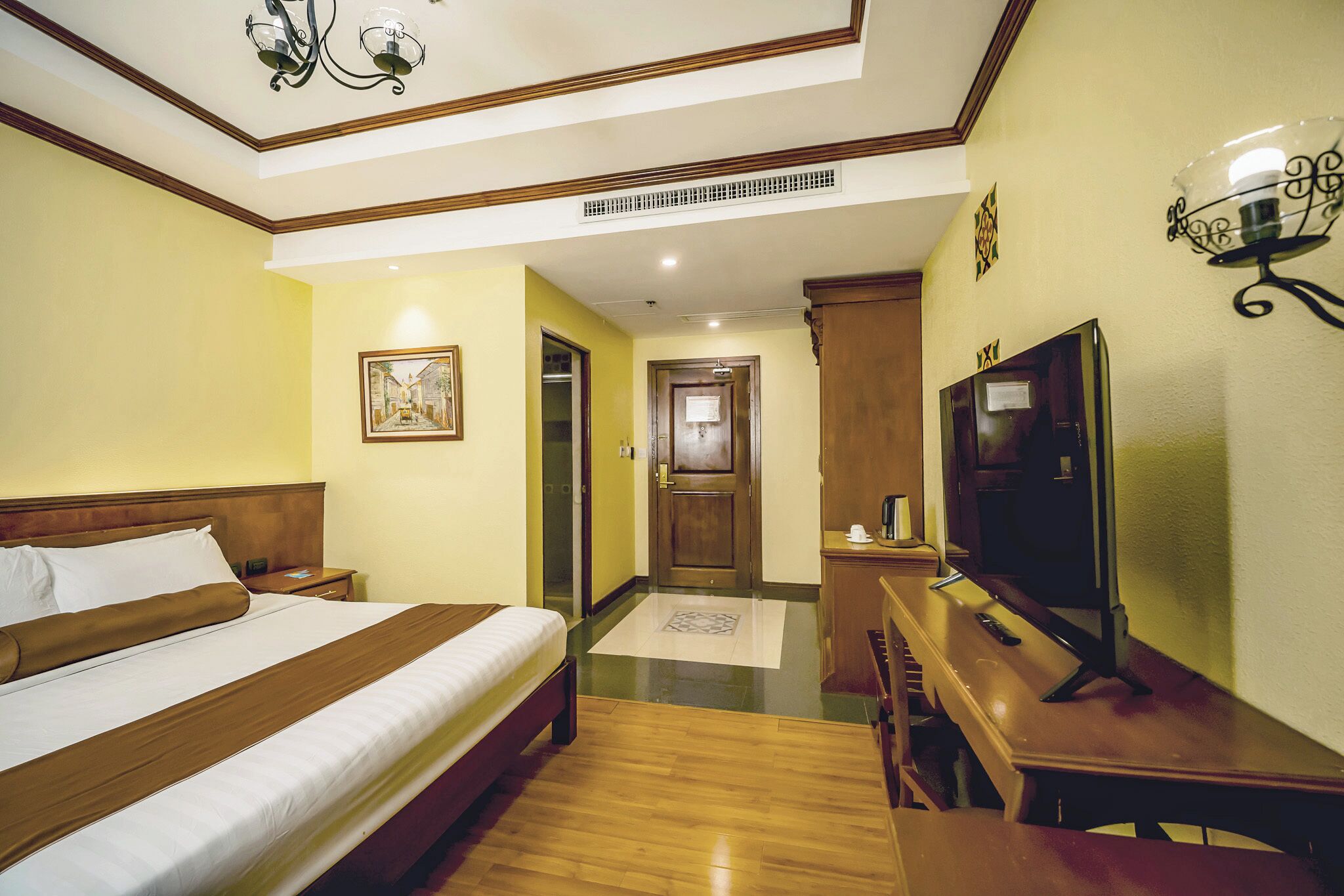 A hotel room with a bed, a desk, a television, and a door leading to a hallway.