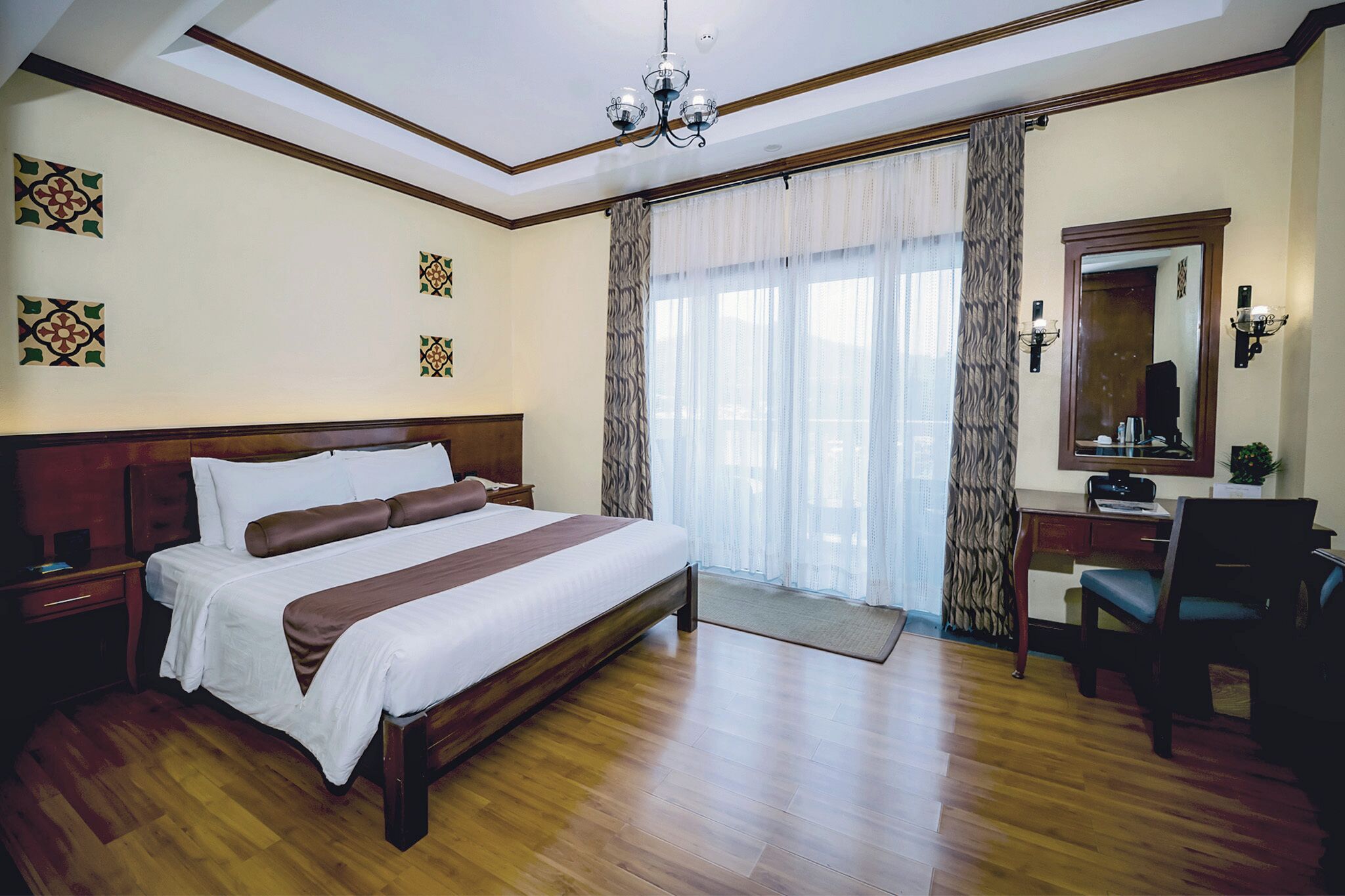 Ein Hotelzimmer mit einem großen Bett, einem Schreibtisch mit Stuhl, einem Spiegel und einer Kandelaber.