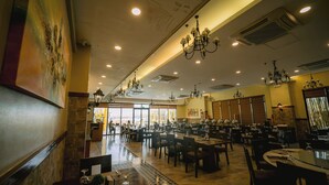Un restaurante espacioso con techos altos, candelabros y vistas amplias a través de grandes ventanales.