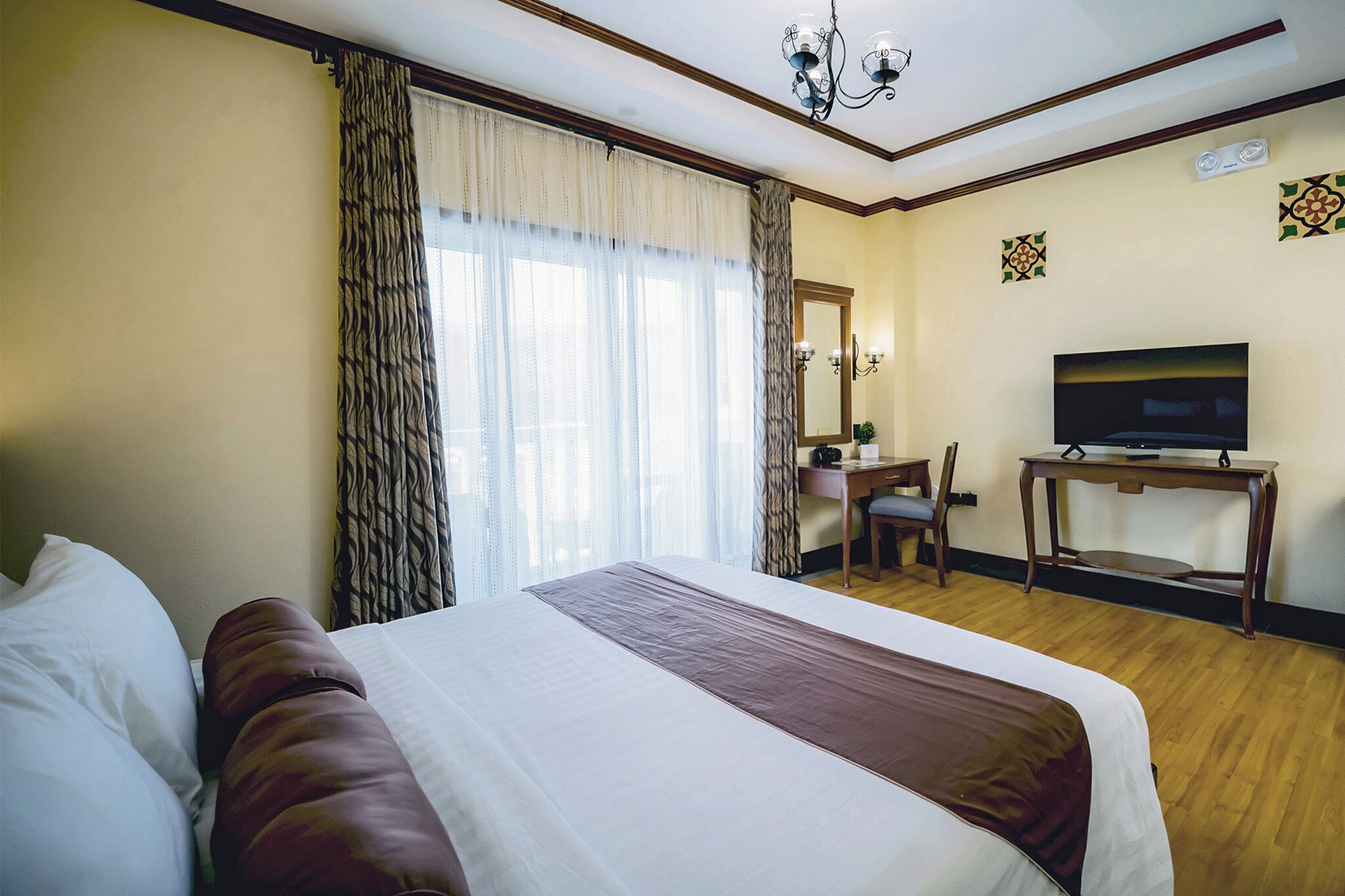 A hotel room with a large bed, a desk with a chair, a television, and a window with curtains.