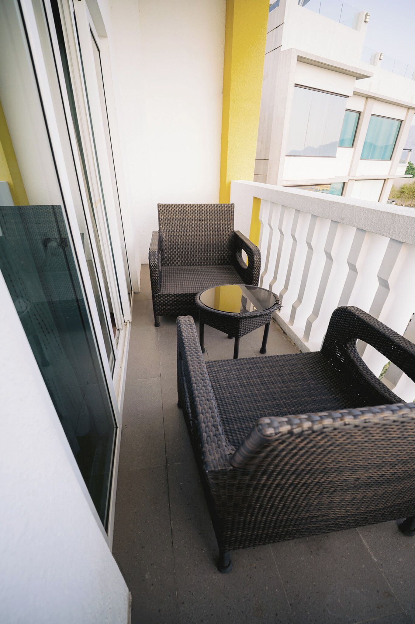 A balcony with wicker furniture, a glass table, and a yellow accent wall.