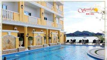 A hotel pool area with a clear view of the sea and mountains in the background.