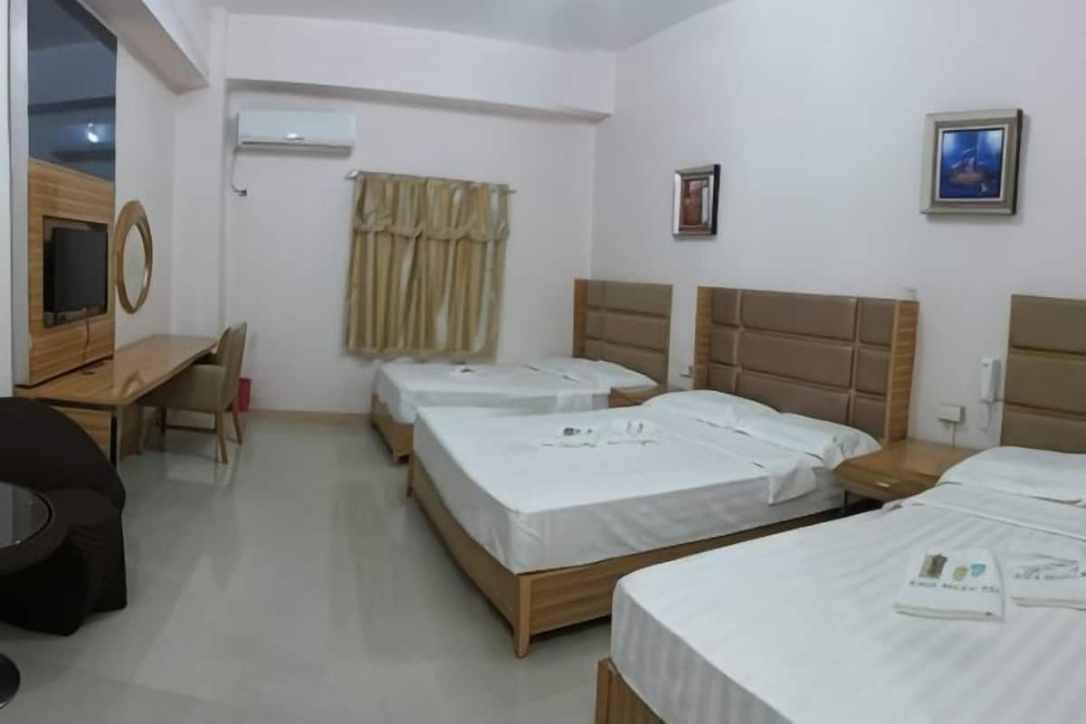 A hotel room with three beds, a desk, a chair, an air conditioning unit, and a television.