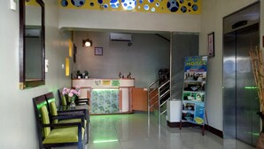 A hotel reception area with a reception desk, a clock, a small plant, and a poster advertising the hotel. - Asia Novo Boutique Hotel - Sorsogon (Sorsogon City)