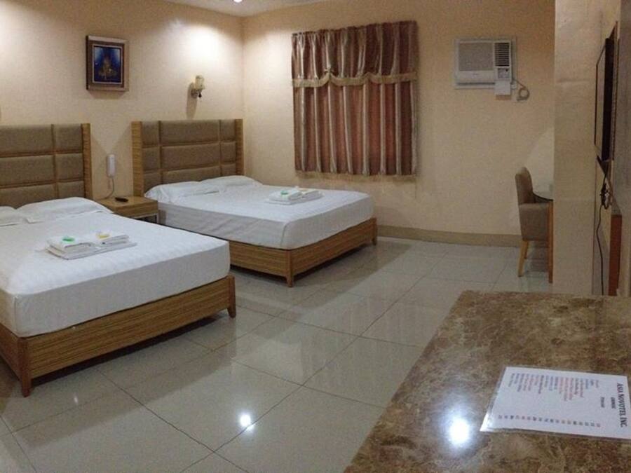 A hotel room with two single beds, a marble table, a chair, a TV, an air conditioning unit, and a framed picture on the wall.