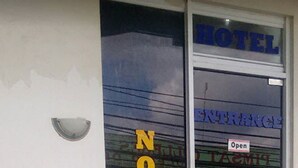 Entrada de hotel com porta de vidro, uma placa indicando 'Aberto' e o nome 'NOVO' refletido no vidro.
