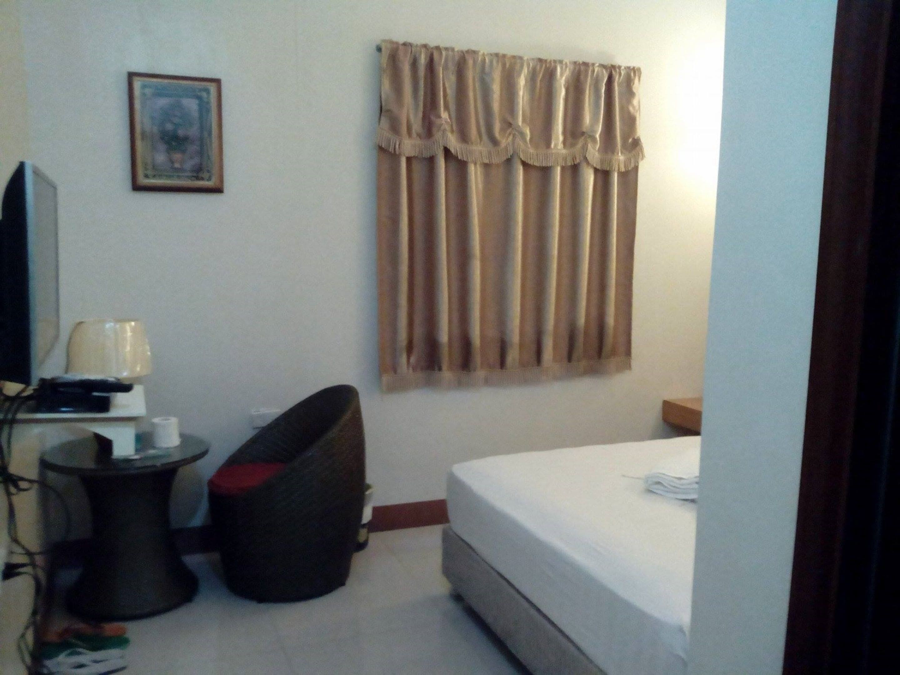 A hotel room with a bed, a small table with a lamp, a chair, and a picture on the wall.