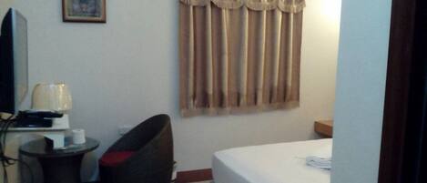 A hotel room with a bed, a small table with a lamp, a chair, and a picture on the wall.