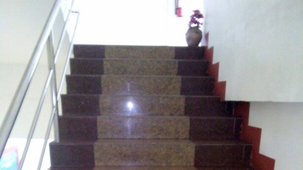 Uma escadaria com degraus alternados em tons escuros e claros, um corrimão de metal e um vaso no último degrau.
